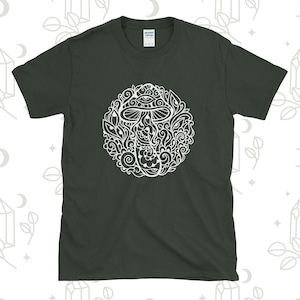 Könnte beinhalten: Ein dunkelgrünes T-Shirt mit einem weißen Motiv eines Pilzes mit Augen und Wirbeln. Der Pilz ist von einem Kreis aus komplizierten Designs umgeben.