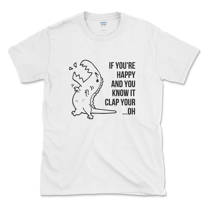Peut inclure: T-shirt blanc avec une illustration noir et blanc d'un dinosaure en train de pleurer. Le texte "IF YOU'RE HAPPY AND YOU KNOW IT CLAP YOUR ...OH" est imprim&eacute; sur le t-shirt.