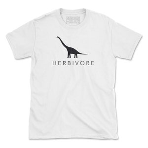 Op de afbeelding: Wit T-shirt met een zwart silhouet van een dinosaurus en het woord "HERBIVORE" gedrukt op de voorkant.