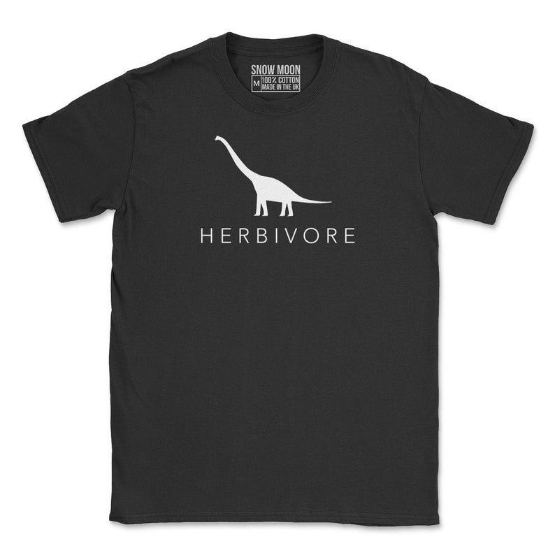 Op de afbeelding: Zwart T-shirt met een wit silhouet van een dinosaurus en het woord "HERBIVORE" gedrukt op de voorkant. Het T-shirt is gemaakt van 100% katoen en is gemaakt in het Verenigd Koninkrijk.