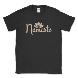 K&ouml;nnte beinhalten: Schwarzes T-Shirt mit dem Wort "Namaste" in beiger Schrift, gekr&ouml;nt von einer Lotusblumen-Grafik. Das Rundhals-T-Shirt ist aus Baumwolle. Das Gildan-Markenetikett ist am Halsausschnitt sichtbar.