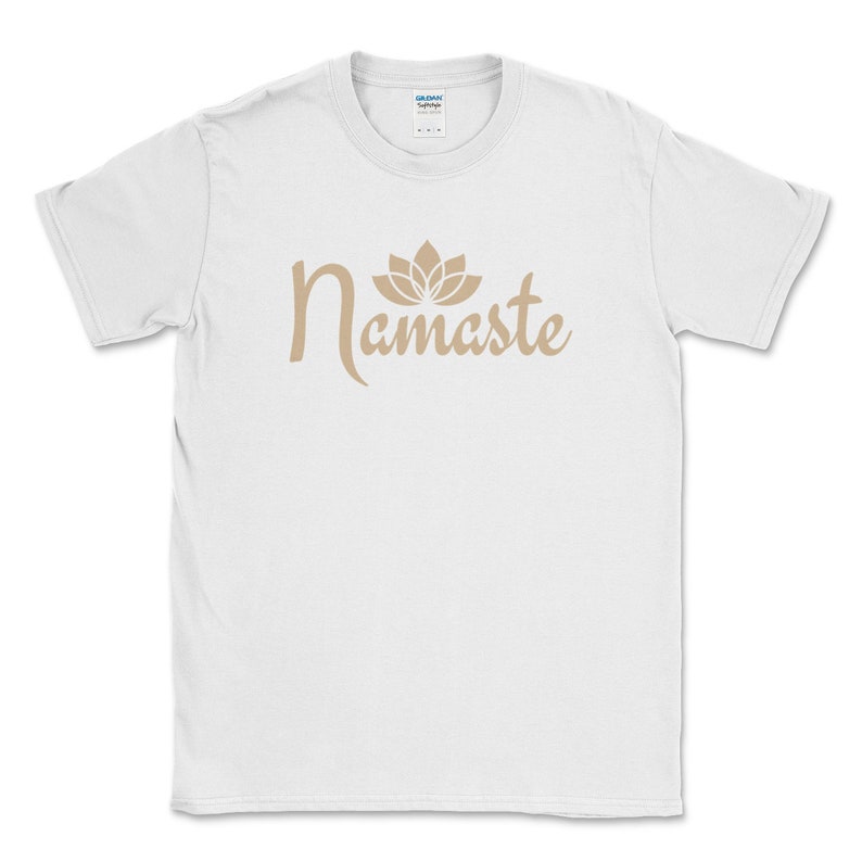 K&ouml;nnte beinhalten: Wei&szlig;es T-Shirt mit dem Wort "Namaste" in hellbrauner Schrift, begleitet von einer Lotusblumen-Grafik. Das Shirt besteht aus einem weichen Material und hat einen Rundhalsausschnitt.