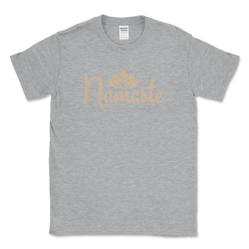 K&ouml;nnte beinhalten: Hellgraues T-Shirt mit dem Wort "Namaste" in hellbrauner Schrift und einem Lotusbl&uuml;ten-Design dar&uuml;ber. Das Shirt besteht aus einem weichen Material und hat einen Rundhalsausschnitt.