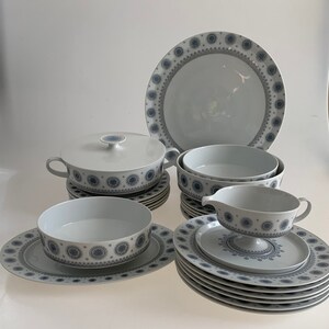 K&ouml;nnte beinhalten: Ein Set aus wei&szlig;em Keramikgeschirr mit einem blauen und grauen geometrischen Muster. Das Set enth&auml;lt eine gro&szlig;e Platte, eine Sch&uuml;ssel, eine Sauciere und mehrere Teller.