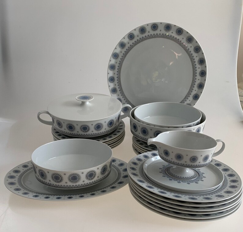 K&ouml;nnte beinhalten: Ein Set aus wei&szlig;em Keramikgeschirr mit einem blauen und grauen geometrischen Muster. Das Set enth&auml;lt eine gro&szlig;e Platte, eine Sch&uuml;ssel, eine Sauciere und mehrere Teller.