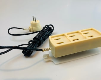 May include: A beige three-outlet power strip with a black cord and a beige plug. The power strip is on a white surface.