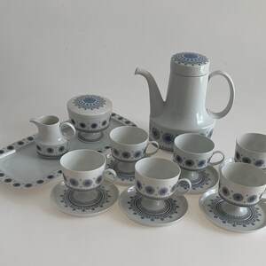 K&ouml;nnte beinhalten: Ein wei&szlig;es Teeservice mit blauen Blumendesigns. Das Set beinhaltet eine Teekanne, eine Zuckerdose, eine Milchk&auml;nnchen und sechs Tassen und Untertassen.