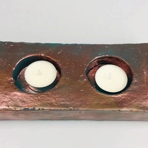 May include: A rectangular concrete candle holder with a copper finish. The holder has two circular depressions for tealight candles.