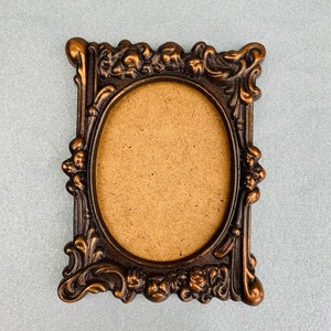 May include: A vintage-style, ornate picture frame with a brown finish and a decorative oval opening. The frame is made of metal and has a detailed floral design.