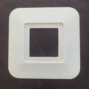 May include: White plastic light switch cover with a decorative geometric pattern around the edge.