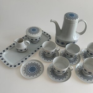 K&ouml;nnte beinhalten: Ein Vintage-Tee-Set mit wei&szlig;er Basis und blau-wei&szlig;em geometrischem Muster. Das Set enth&auml;lt eine Teekanne, eine Milchk&auml;nnchen, eine Zuckerdose, sechs Tassen und sechs Untertassen. Das Set befindet sich auf einem wei&szlig;en Tablett.