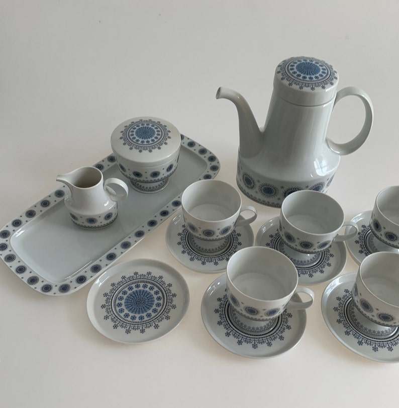K&ouml;nnte beinhalten: Ein Vintage-Tee-Set mit wei&szlig;er Basis und blau-wei&szlig;em geometrischem Muster. Das Set enth&auml;lt eine Teekanne, eine Milchk&auml;nnchen, eine Zuckerdose, sechs Tassen und sechs Untertassen. Das Set befindet sich auf einem wei&szlig;en Tablett.