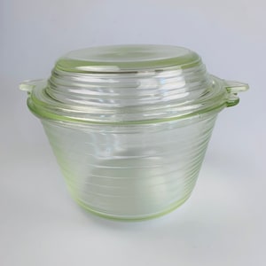 May include: A clear glass storage container with a lid. The container has a ribbed design and a pale green tint. The lid is also clear glass and has a ribbed design.