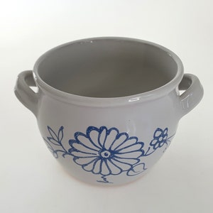 Puede incluir: Maceta de cerámica blanca con diseño floral azul. La maceta tiene dos asas y una forma redondeada.