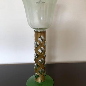 May include: A clear glass vase with a green base and a gold metal band around the middle. The vase is decorated with a series of small glass spheres. The vase has the text "Villeroy & Boch 1748" on the side.
