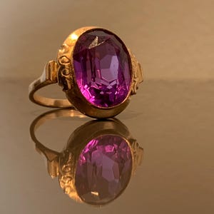 Puede incluir: Un anillo de oro con una piedra preciosa ovalada de color púrpura engastada en un engaste decorativo.