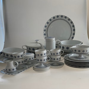 K&ouml;nnte beinhalten: Ein Set aus wei&szlig;em Porzellan-Geschirr mit einem blauen und grauen Blumenmuster. Das Set enth&auml;lt Teller, Schalen, Tassen, Untertassen, eine Teekanne, eine Zuckerdose, eine Milchk&auml;nnchen und eine Servierplatte.