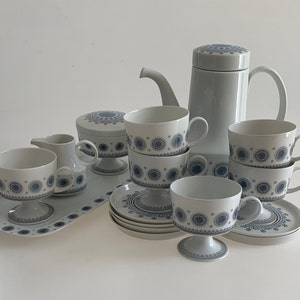 K&ouml;nnte beinhalten: Ein wei&szlig;es Teeservice mit blauen und grauen Blumenmustern. Das Set beinhaltet eine Teekanne, eine Milchk&auml;nnchen, eine Zuckerdose und vier Tassen mit Untertassen.