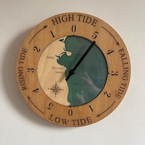 May include: A wooden tide clock featuring a map of Dublin, Dún Laoghaire, and Shankill. The clock face has a black hand pointing to the high tide mark. The clock face is labelled "High Tide", "Low Tide", "Rising Tide", and "Falling Tide".