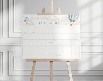 May include: A light-colored calendar on a wooden easel, featuring a design with hot air balloons and the text "Guess the arrival of BABY ALDER." The calendar grid is for tracking the baby's due date.