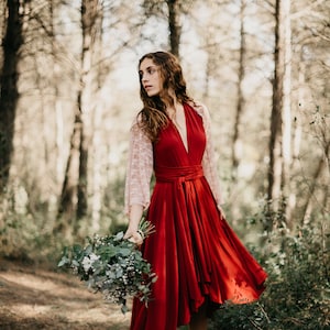 Könnte beinhalten: Eine Frau in einem roten Kleid mit weißen Spitzenärmeln steht in einem Wald. Sie hält einen Strauß weißer Blumen und Grünzeug in der Hand. Sie trägt braune Stiefel.