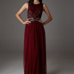 Könnte beinhalten: Ein burgunderfarbenes, ärmelloses Maxikleid mit einem Paillettenoberteil und einem Tüllrock. Das Kleid hat einen silbernen Gürtel.