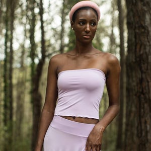 Peut inclure: Une femme portant un haut sans bretelles et une jupe assortis de couleur lilas clair. Elle porte un bandeau rose et se tient dans une forêt.