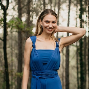 May include: A woman wearing a royal blue convertible dress with a knotted strap detail. The dress is made of a soft, stretchy fabric and can be styled in many different ways.
