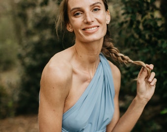 May include: A woman with long blonde hair wearing a light blue one-shoulder dress. She is smiling and looking at the camera.