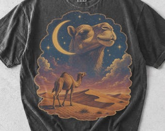 Può includere: Una t-shirt a maniche corte grigio antracite con una stampa grafica di un paesaggio desertico, un cammello che cammina sulle dune di sabbia sotto un cielo stellato con una luna crescente e una testa di cammello eterea tra le nuvole.
