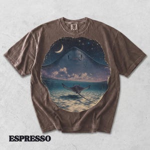 Pode incluir: Uma t-shirt castanha de manga curta com um gr&aacute;fico circular de uma raia a nadar num oceano pouco profundo sob um c&eacute;u noturno com uma lua crescente e estrelas. A palavra ESPRESSO est&aacute; impressa em letras mai&uacute;sculas pretas abaixo.