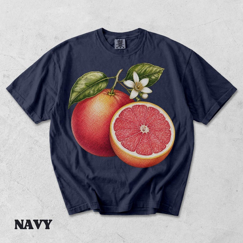 Puede incluir: Una camiseta azul marino de manga corta con una ilustraci&oacute;n bot&aacute;nica de un pomelo entero, un pomelo cortado por la mitad con segmentos rosados visibles, hojas verdes y una flor blanca centrada en el pecho. Cuello redondo.
