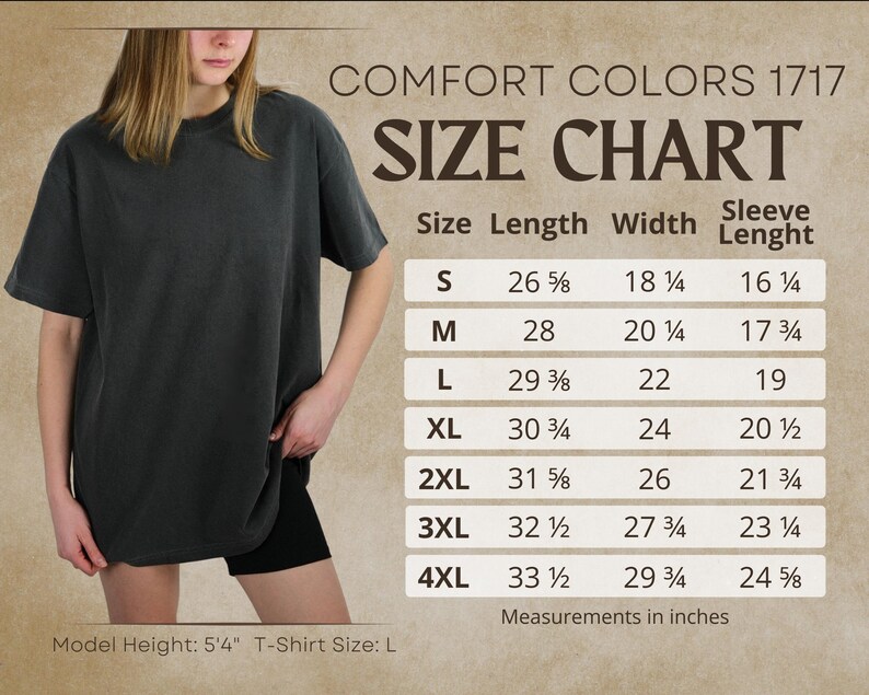 Pode incluir: Uma tabela de tamanhos Comfort Colors 1717 exibindo medidas em polegadas para tamanhos de S a 4XL. A tabela lista comprimento, largura e comprimento da manga. Uma camiseta cinza escuro &eacute; exibida com altura do modelo 5'4" e tamanho L.