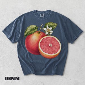 Puede incluir: Una camiseta de manga corta color azul pizarra con una ilustraci&oacute;n gr&aacute;fica de un pomelo entero, un pomelo cortado por la mitad con interior rosa y una flor de c&iacute;trico blanca con hojas verdes en el centro. La camiseta tiene cuello redondo.