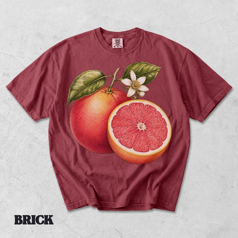 Puede incluir: Una camiseta de manga corta color rojo ladrillo con un estampado gr&aacute;fico de un pomelo entero, un pomelo cortado por la mitad, hojas verdes y una flor blanca. La etiqueta interior del cuello muestra el texto Comfort Colors.
