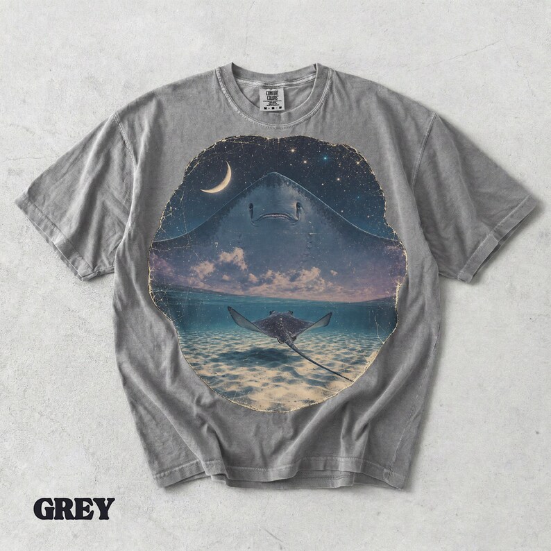 Pode incluir: Uma t-shirt cinzenta de manga curta com uma impress&atilde;o gr&aacute;fica circular de uma raia grande a nadar num oceano l&iacute;mpido sob um c&eacute;u noturno com uma lua crescente e estrelas. O design mostra uma segunda raia mais pequena debaixo de &aacute;gua.