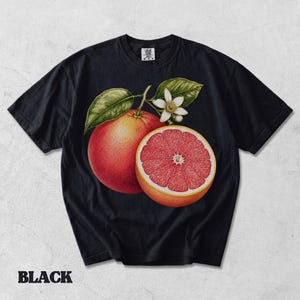 Puede incluir: Una camiseta negra de manga corta con un gr&aacute;fico central de un pomelo entero y otro cortado por la mitad con interior rosa, acompa&ntilde;ado de hojas verdes y una peque&ntilde;a flor de c&iacute;trico blanca. La prenda cuenta con un cuello redondo cl&aacute;sico.