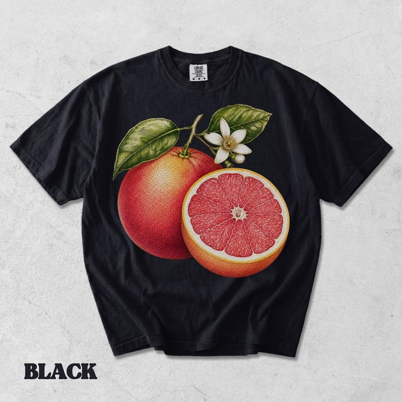 Puede incluir: Una camiseta negra de manga corta con un gr&aacute;fico central de un pomelo entero y otro cortado por la mitad con interior rosa, acompa&ntilde;ado de hojas verdes y una peque&ntilde;a flor de c&iacute;trico blanca. La prenda cuenta con un cuello redondo cl&aacute;sico.