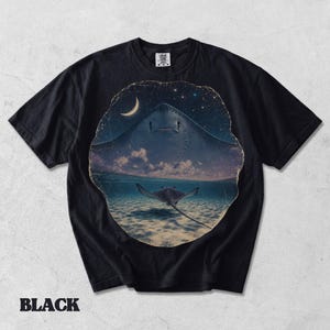 Pode incluir: Uma t-shirt preta de manga curta com uma estampa gr&aacute;fica circular. O design mostra a silhueta de uma raia grande contra um c&eacute;u noturno estrelado com uma lua crescente, acima de uma raia menor a nadar em &aacute;gua do mar l&iacute;mpida.