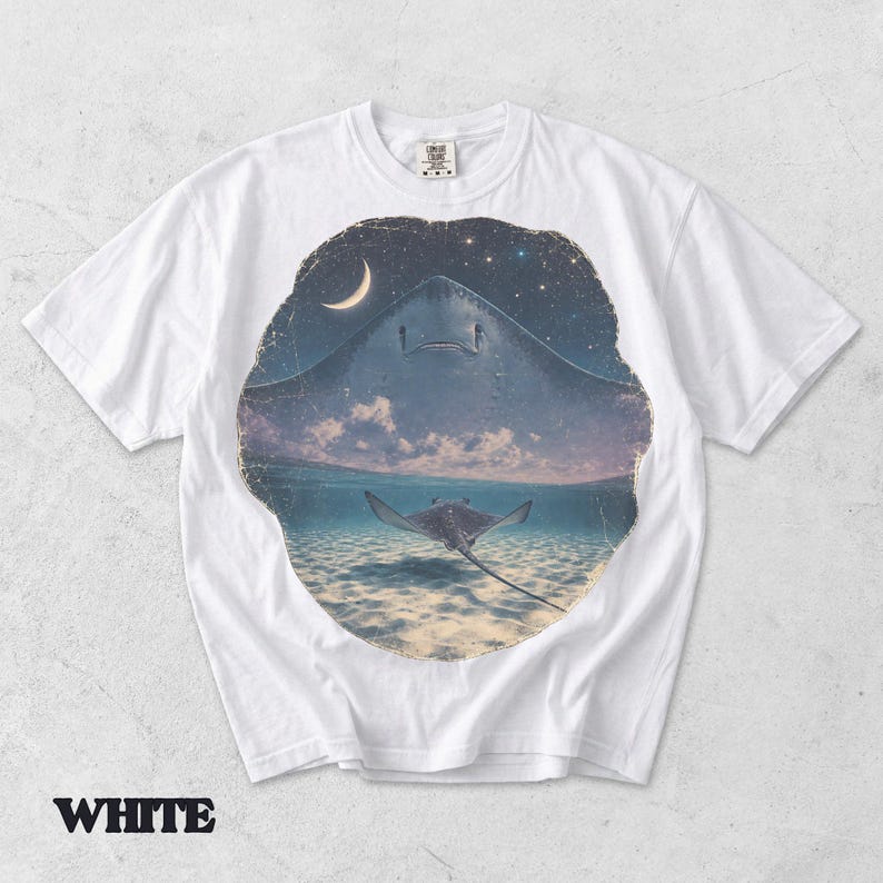 Pode incluir: Uma t-shirt branca de manga curta com uma impress&atilde;o gr&aacute;fica circular. O design mostra a silhueta de uma raia grande contra um c&eacute;u estrelado com uma lua crescente, transicionando para uma cena subaqu&aacute;tica com uma raia mais pequena.