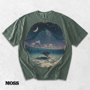 Pode incluir: Uma t-shirt de manga curta verde musgo com uma impress&atilde;o gr&aacute;fica circular. O design mostra a silhueta de uma raia grande contra um c&eacute;u estrelado acima de uma raia menor a nadar em &aacute;gua l&iacute;mpida com uma lua crescente vis&iacute;vel.