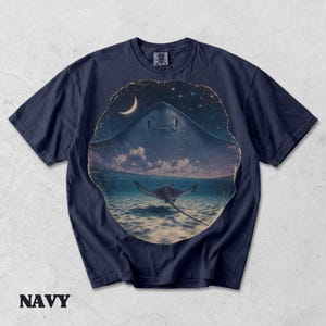 Pode incluir: Uma t-shirt de manga curta azul-marinho com uma estampa gr&aacute;fica circular. O design mostra a silhueta de uma raia grande contra um c&eacute;u noturno estrelado com uma lua crescente e uma raia menor nadando na &aacute;gua do oceano abaixo.