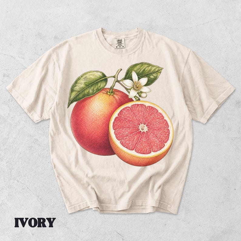 Puede incluir: Una camiseta de manga corta color marfil con una ilustraci&oacute;n bot&aacute;nica de un pomelo entero y medio pomelo con hojas verdes y una flor blanca. El gr&aacute;fico est&aacute; centrado en el pecho y la camiseta tiene un cuello redondo.