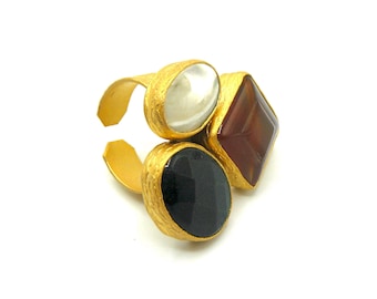 May include: Gold ring with three stones: a white oval, a black oval, and a brown square.