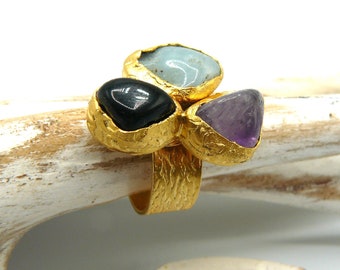 May include: Gold ring featuring three stones: a black stone, a light blue stone, and a purple stone.