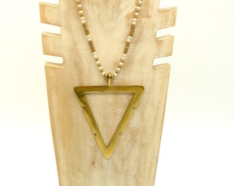 Peut inclure: Un collier avec un pendentif triangle en or et une chaîne de perles blanches. Le collier est présenté sur un mannequin en bois.