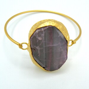 Puede incluir: Un brazalete de oro con una gran piedra preciosa facetada de color púrpura engastada en un engaste de oro.