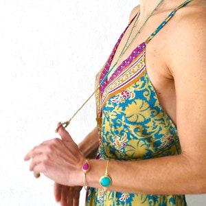 May include: A woman wearing a yellow and blue floral print dress with a gold chain necklace and turquoise and pink gemstone bracelets.