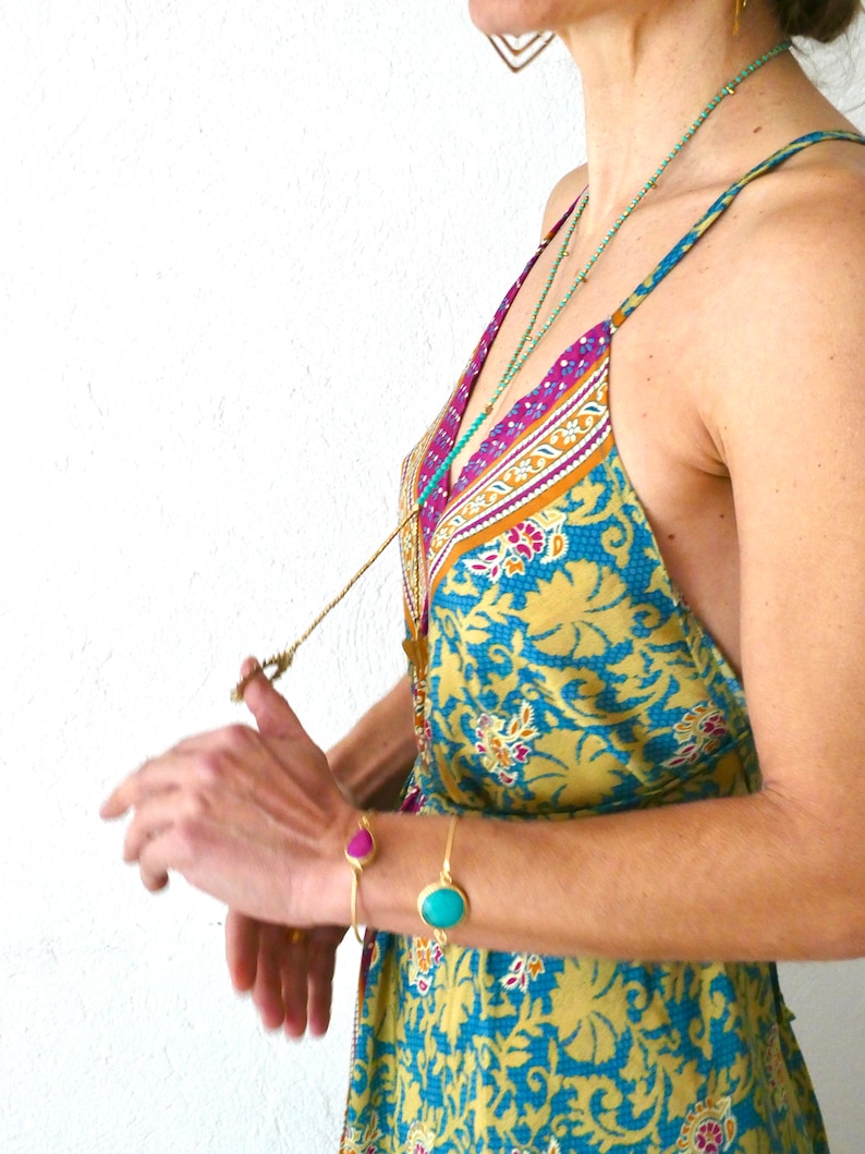 May include: A woman wearing a yellow and blue floral print dress with a gold chain necklace and turquoise and pink gemstone bracelets.