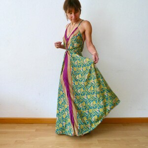 May include: A woman wearing a long, flowing maxi dress with a floral print in shades of green, yellow, and pink. The dress has a V-neckline and a tie at the waist.
